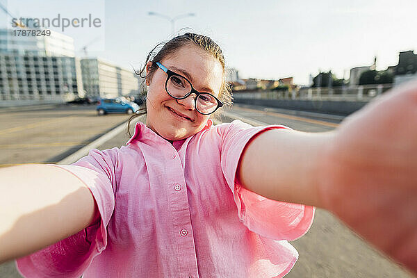 Lächelndes Teenager-Mädchen mit Down-Syndrom macht Selfie auf der Straße