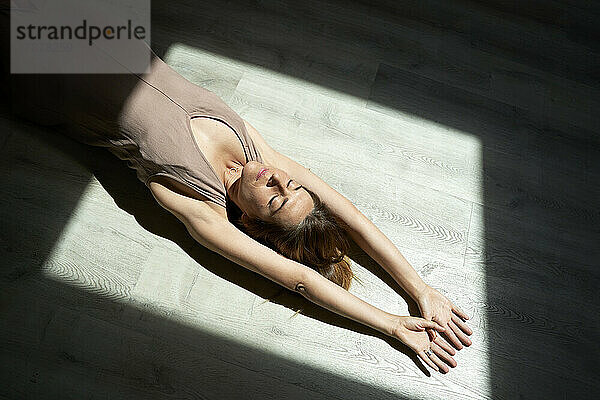 Frau liegt mit erhobenen Armen entspannt auf dem Boden im Sonnenlicht
