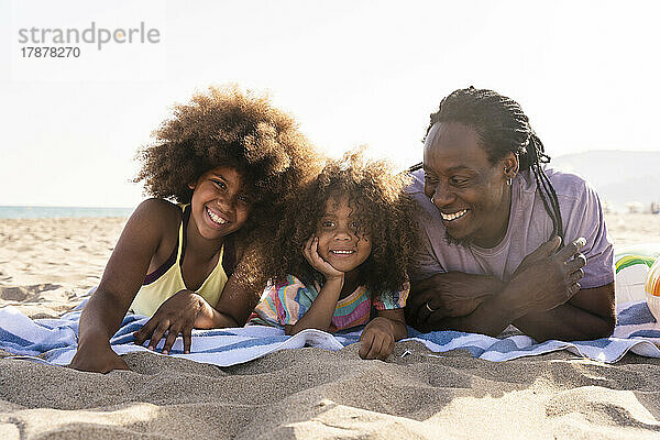 Lächelnder Vater mit Töchtern  die zusammen am Strand liegen