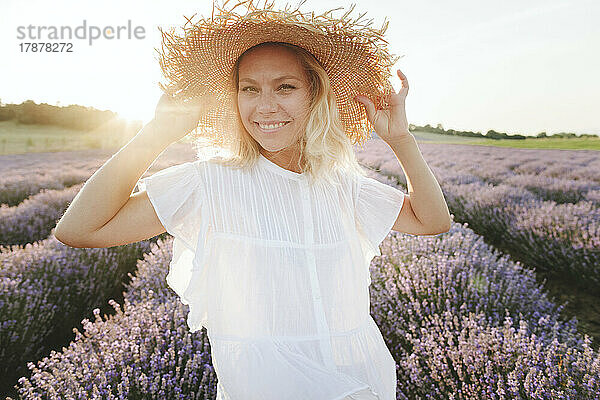 Lächelnde Frau mit Strohhut steht im Lavendelfeld