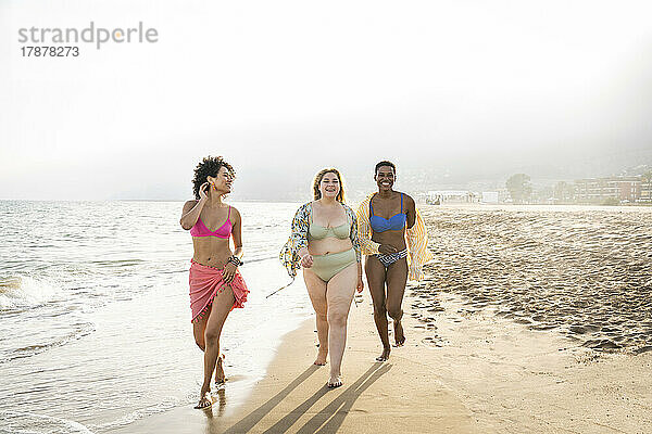 Gemischtrassige Frauen gehen an einem sonnigen Tag am Strand spazieren