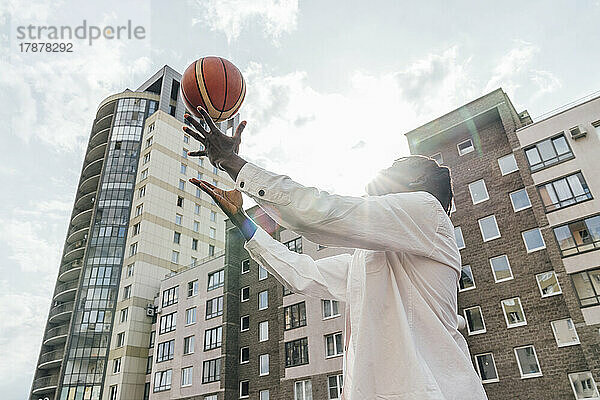 Junger Mann wirft an einem sonnigen Tag Basketball vor Gebäuden