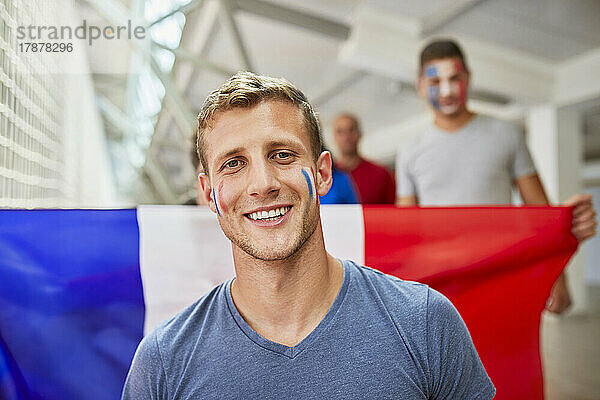 Lächelnder Mann mit aufgemalter französischer Flagge im Gesicht bei einer Sportveranstaltung im Stadion