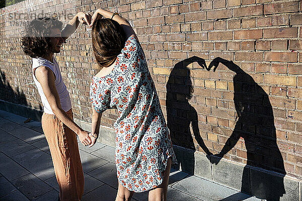 Junges Paar formt an einem sonnigen Tag vor der Wand ein Herz