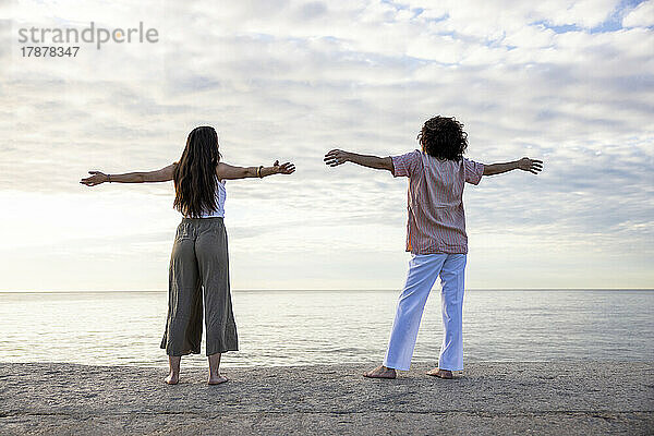 Couple with arms outstretched standing at pier