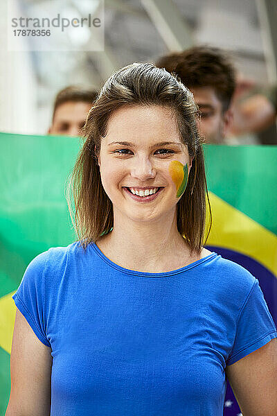 Lächelnde Frau mit aufgemalter Brasilien-Flagge im Gesicht