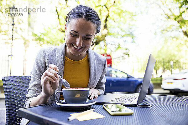 Glückliche Geschäftsfrau genießt Kaffee mit Laptop im Straßencafé