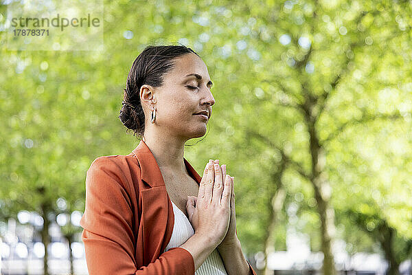 Geschäftsfrau mit gefalteten Händen meditiert im Park