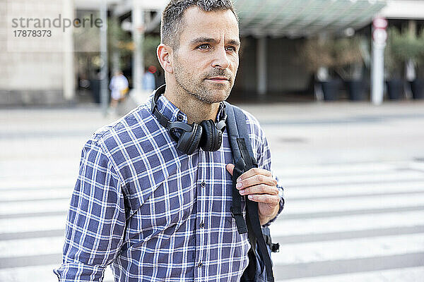 Reifer Mann mit kabellosen Kopfhörern und Rucksack überquert die Straße