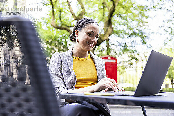 Lächelnde Geschäftsfrau benutzt Laptop im Straßencafé