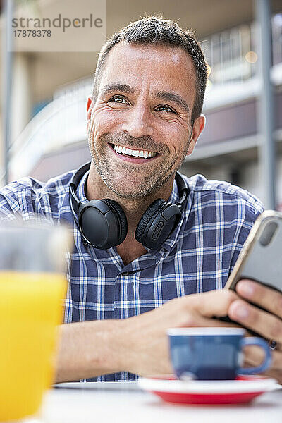 Fröhlicher reifer Mann mit Smartphone sitzt im Straßencafé