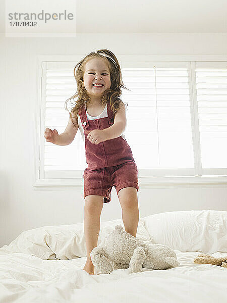 Lächelndes Mädchen (2-3) springt aufs Bett
