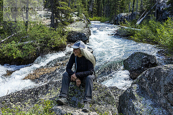 Vereinigte Staaten  Idaho  Stanley  Ältere blonde Frau wandert an einem rauschenden Bach in den Bergen in der Nähe von Sun Valley