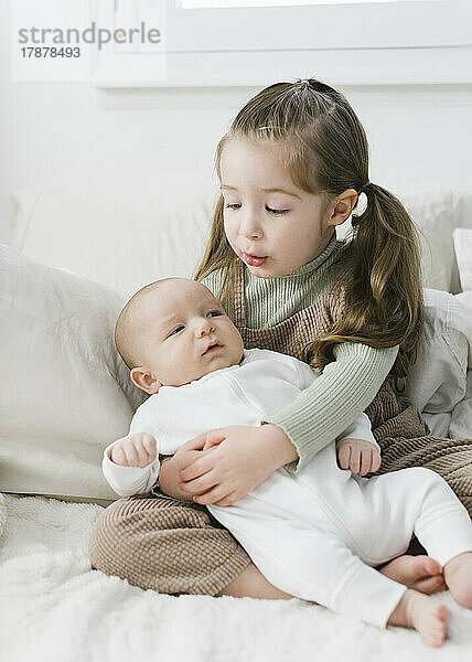 Mädchen (2-3) umarmt neugeborenen Bruder (0-1 Monat) im Bett