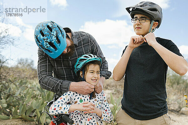 Vater und Kinder (8-9  14-15) passen Fahrradhelme an