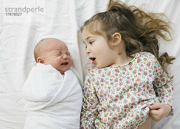 Draufsicht auf ein Mädchen (2–3) mit ihrem neugeborenen Bruder (0–1 Monat) im Bett