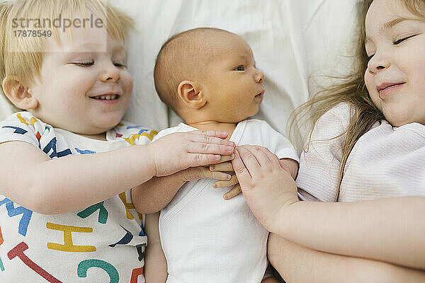 Bruder und Schwester (2-3) mit neugeborenem Jungen (0-1 Monat) im Bett