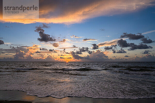 Dramatischer Sonnenaufgangshimmel über Meer und Strand