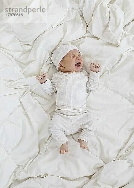Draufsicht auf einen neugeborenen Jungen (0–1 Monat)  der weinend auf dem Bett liegt
