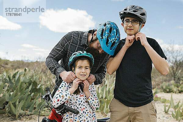 Vater und Kinder (8-9  14-15) passen Fahrradhelme an