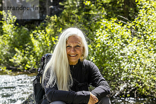 Vereinigte Staaten  Idaho  Stanley  Ältere blonde Frau ruht sich am rauschenden Bach in der Nähe von Sun Valley aus