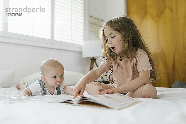 Mädchen (2-3) liest ihrem kleinen Bruder (6-11 Monate) ein Buch vor