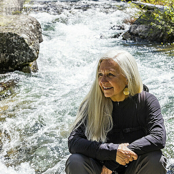 Vereinigte Staaten  Idaho  Stanley  Ältere blonde Frau ruht sich am rauschenden Bach in der Nähe von Sun Valley aus