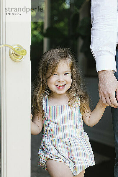 Porträt eines lächelnden Mädchens (2-3)  das zu Hause in der Tür die Hand seines Vaters hält