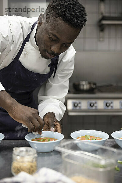 Männlicher Koch wischt Schüssel mit Suppe bei der Arbeit im Restaurant ab