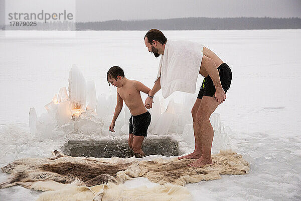 Mann hält die Hand seines Sohnes beim Eisbaden auf einem zugefrorenen See in voller Länge