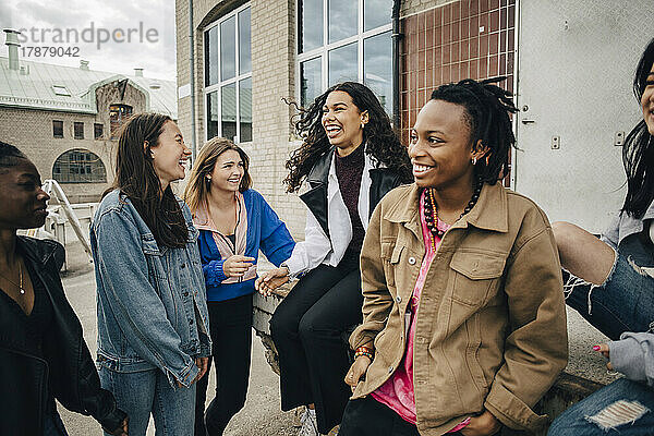 Glückliche multirassische junge Freunde unterhalten sich vor einem Gebäude
