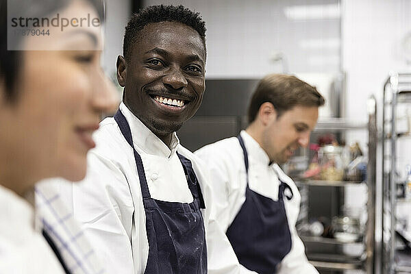 Porträt eines lächelnden Kochs inmitten von Kollegen  die in der Küche eines Restaurants arbeiten