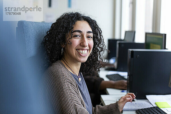 Seitenansicht einer glücklichen Geschäftsfrau  die am Schreibtisch im Büro sitzt