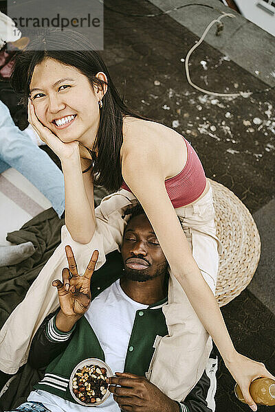 Porträt einer glücklichen jungen Frau mit einem männlichen Freund  der auf einer Dachterrassenparty das Friedenszeichen macht