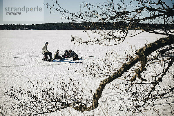 Väter mit Söhnen beim Eisfischen an einem sonnigen Tag im Winter