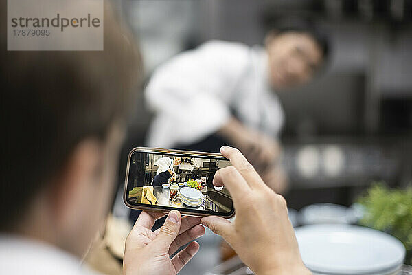 Koch fotografiert Kollegen bei der Zubereitung von Speisen im Restaurant