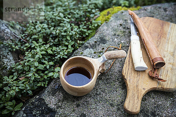 Tasse Tee mit Messer und Schneidebrett auf einem Felsen