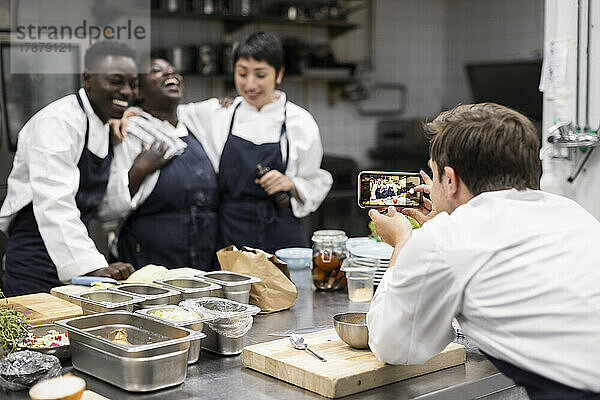 Chefkoch fotografiert fröhliche Kollegen in der Restaurantküche