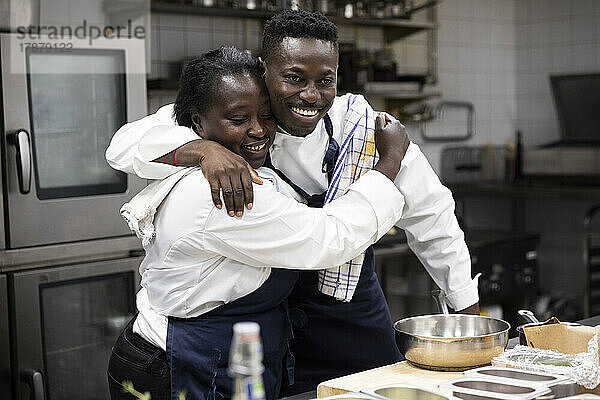 Lächelnde Köche  die sich umarmen  während sie in der Küche eines Restaurants stehen