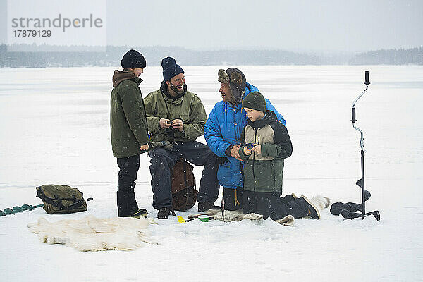 Fröhliche männliche Freunde vergnügen sich mit ihren Söhnen am zugefrorenen See
