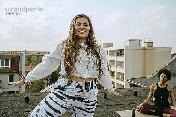 Porträt einer lächelnden jungen Frau  die mit einem Freund auf dem Dach Yoga übt
