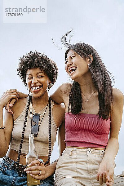 Fröhliche junge Frauen  die lachend vor dem Himmel sitzen