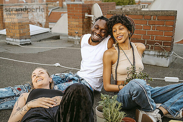 Junger Mann lacht  während er mit Freundinnen auf dem Dach sitzt
