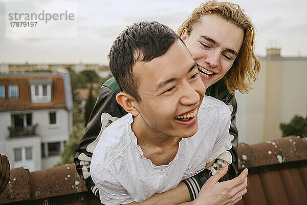 Fröhlicher junger Mann  der seinen Freund umarmt  während er gemeinsam auf dem Dach sitzt