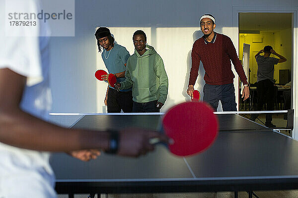 Aufgeregte Freunde spielen Tischtennis im Spielzimmer