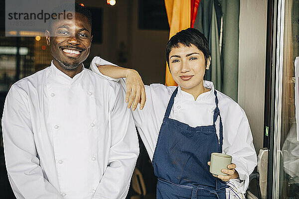 Porträt von lächelnden multirassischen Köchen  die am Eingang eines Restaurants stehen
