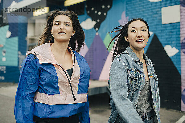 Lächelnde multirassische junge Frauen  die beim Gehen auf der Straße wegschauen
