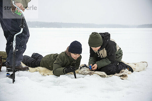 Jungen in warmer Kleidung beim Eisfischen auf einem zugefrorenen See in den Ferien
