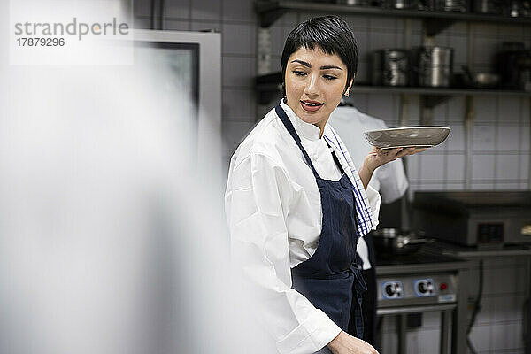 Koch mit kurzen Haaren trägt Teller bei der Arbeit in der Restaurantküche