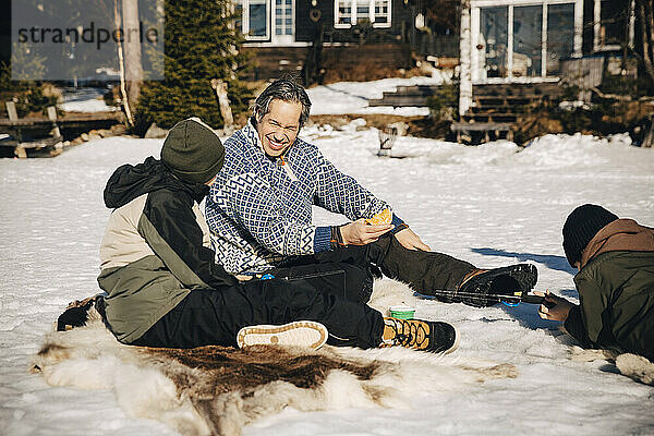 Lächelnder Vater im Gespräch mit seinem Sohn beim Angeln im Schnee liegend an einem sonnigen Tag